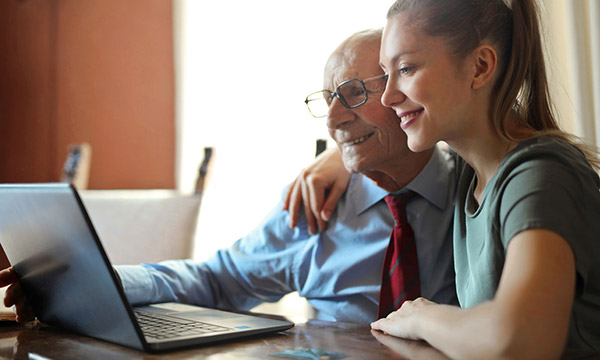 Foto: Ein alter Mann und ein Mädchen sitzen lächelnd vor einem Laptop.