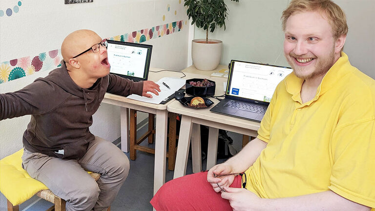 Foto: Kognitiv beeinträchtigte Person und Tester sitzen jeweils an einem Laptop. 