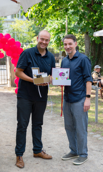 2 Männer lächeln in die Kamera. Überreichung eines Geschenks