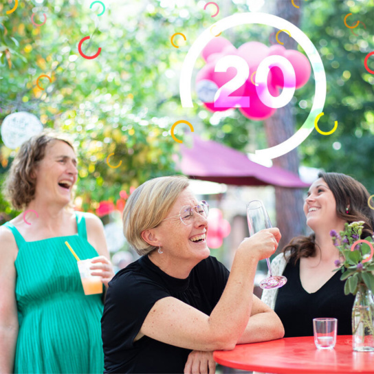 3 Frauen stehend lachend an einem Tisch mit Getränken in der Hand