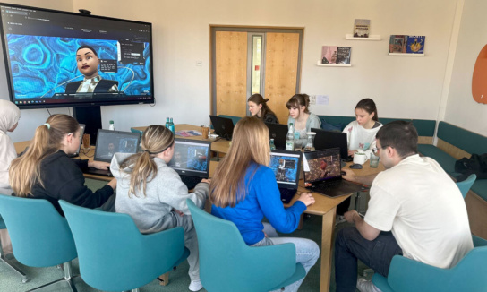 Girls Day: Gruppe von Mädchen und Mitarbeiter von Sandstein sitzen an Rechnern