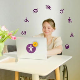 Lächelnde Frau sitzt im Rollstuhl an einem Schreibtisch. Vor ihr ein Laptop. Auf dem Foto sind Icons im Kreis angeordnet, die das Thema Barrierefreiheit behandeln.