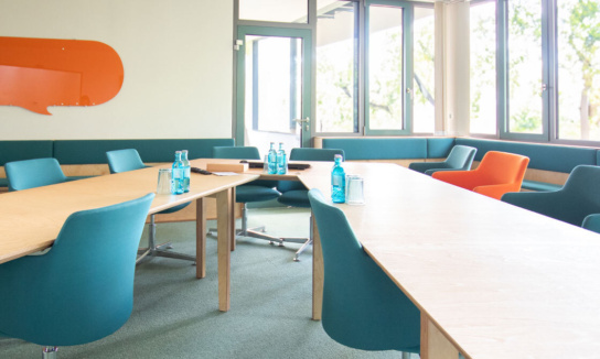 Besprechungsraum Obergeschoss: Blick auf die V-förmig angeordneten Tische und Fenster im Hintergrund