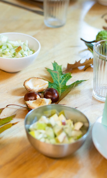 Detail auf dem Tisch: Blätter und Kastanien als Deko. Eine kleine Schüssel Salat daneben.
