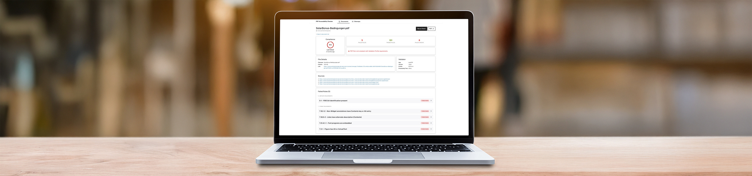 Foto: Laptop mit geöffneter PDF-Prüfsoftware auf einer Holzoberfläche vor unscharfem Hintergrund