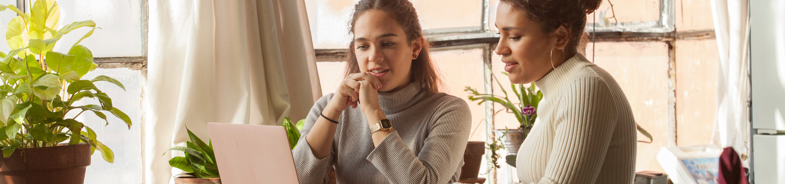 Zwei Frauen sitzen zusammen an einem Tisch und schauen interessiert auf einen Laptop