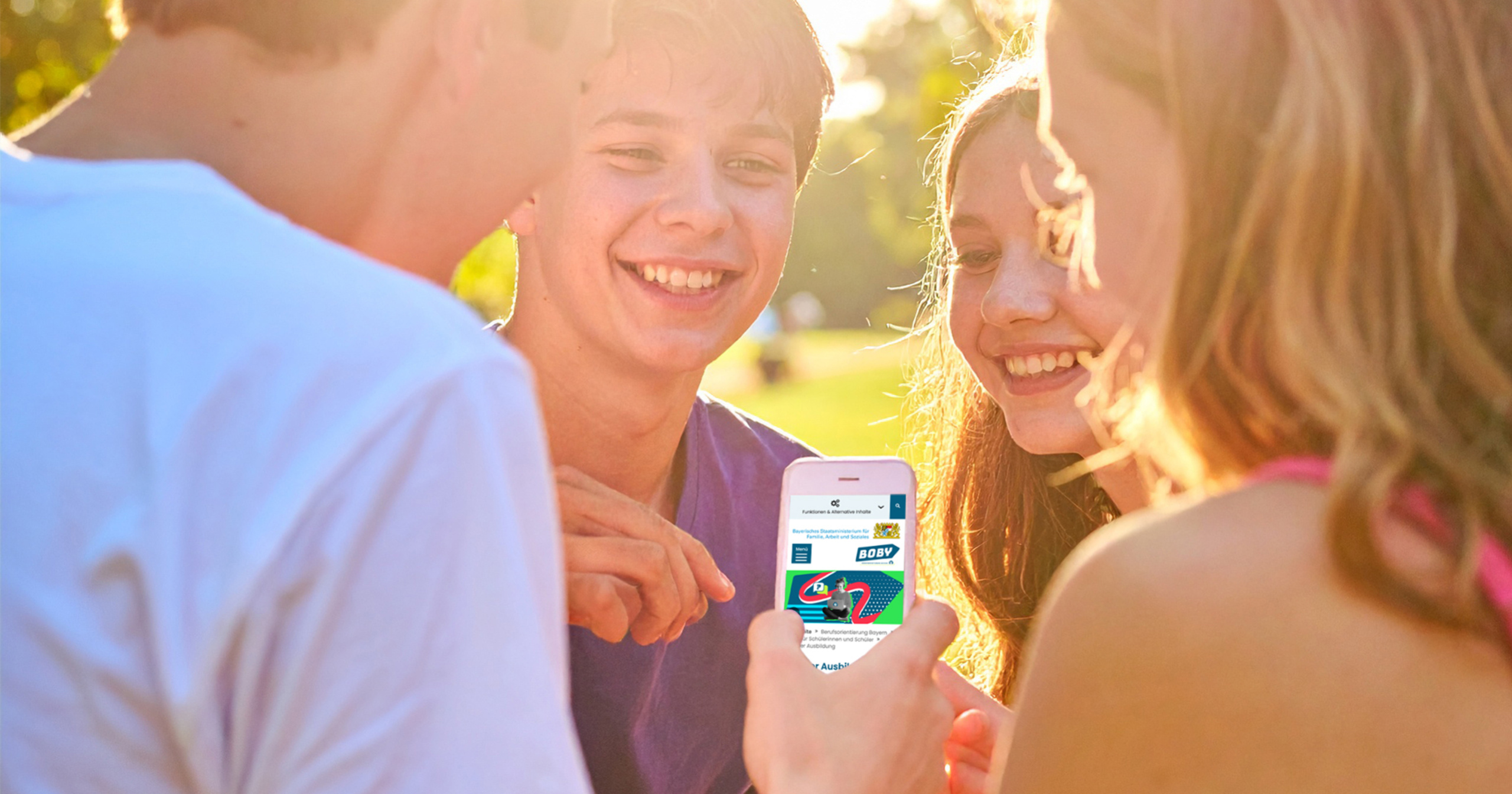 Foto: Jugendliche schauen gemeinsam lachend auf ein Smartphone mit geöffneter Boby-Webseite im Sonnenlicht