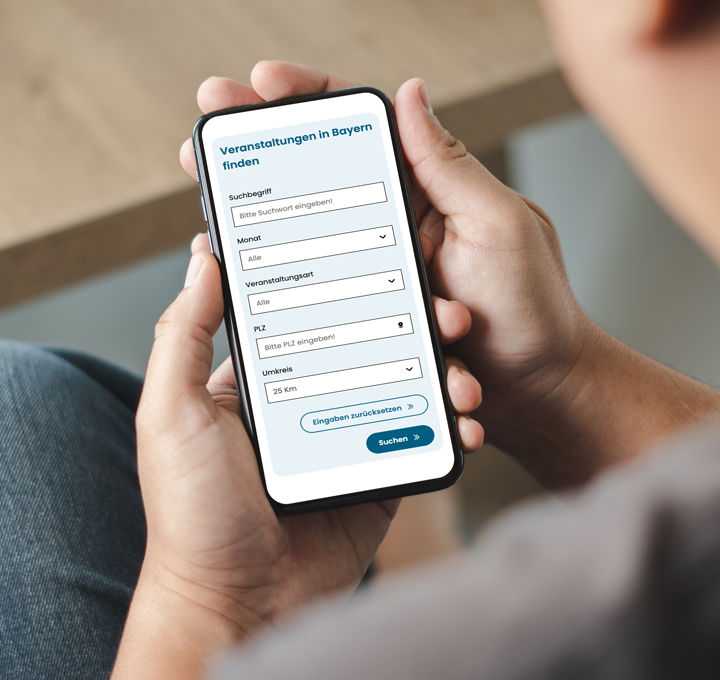 Foto: Person hält Smartphone mit geöffneter Veranstaltungs-Suchmaske für Bayern in der Hand
