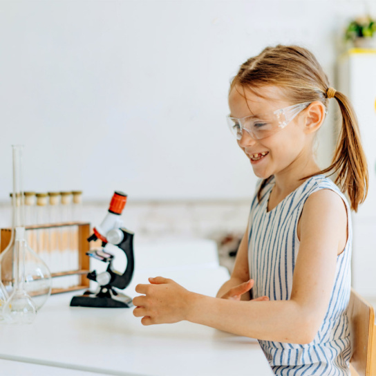 Grafik: Mädchen sitzt am Tisch auf dem ein Mikroskop steht.