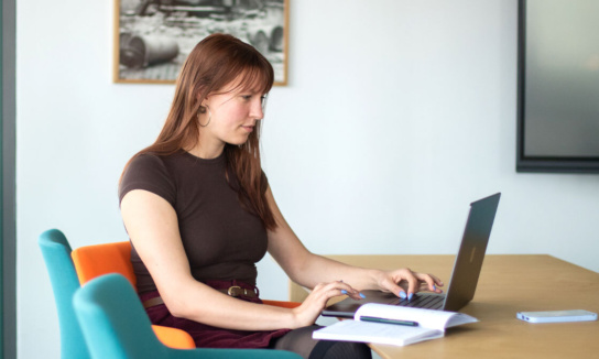 Frau sitzt am Tisch und arbeitet am Laptop