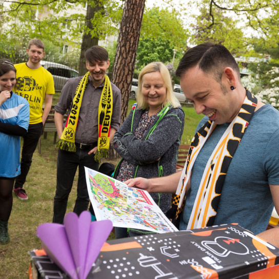 Foto: Eine Mann packt ein Geschenk aus und andere Personen schauen zu