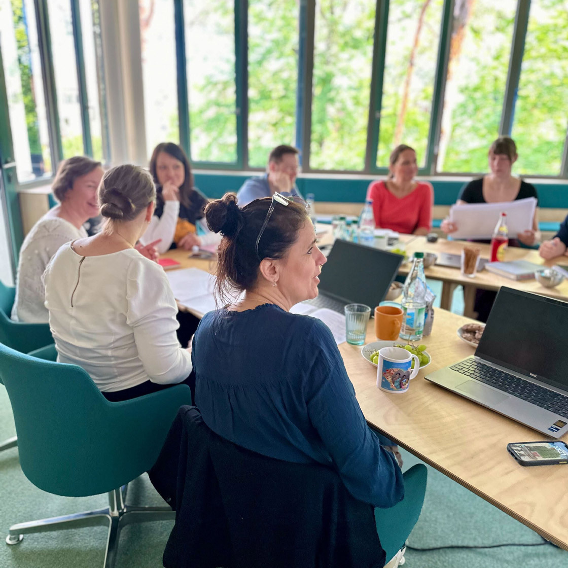 In einem Besprechungsraum mit großen Fenstern sitzen Mitarbeitende der Firma Sandstein zusammen bei einem Meeting