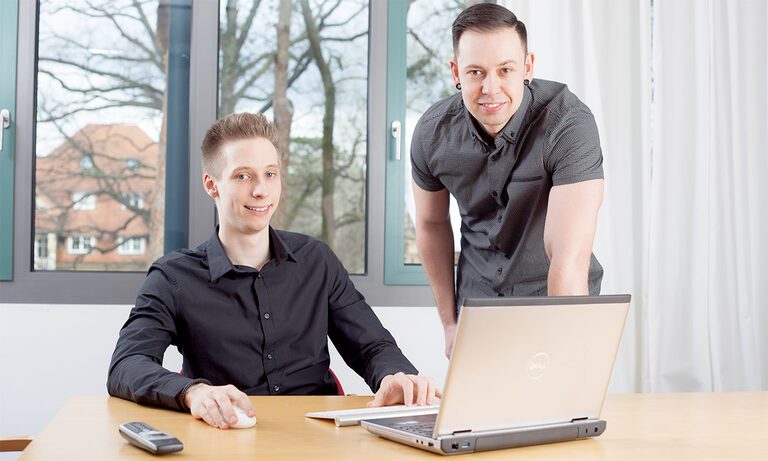 Foto: zwei lächelnde Männer an einem Laptop