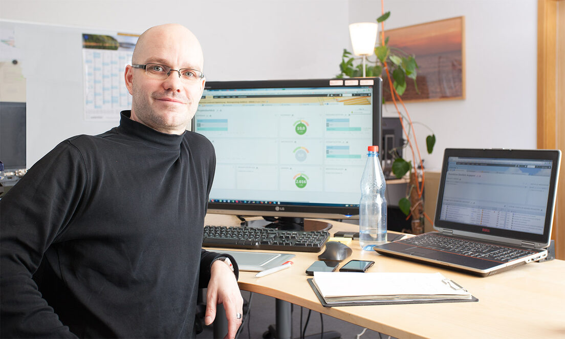 Sandstein Neue Medien sucht Projektmanager (m/w) Foto: Mann lächelnd, in einem Büro