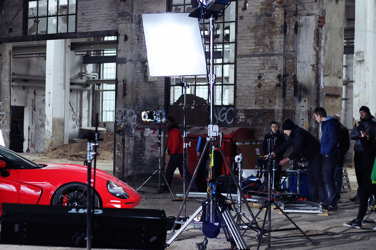 Foto: Ein Filmset mit einigen Menschen und einem modernen Auto.