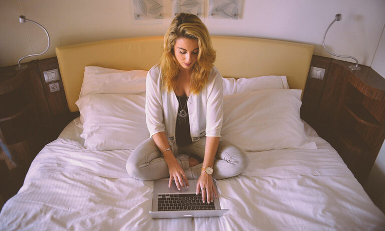 Foto: Frau sitzt auf einem Bett und bedient einen Laptop.