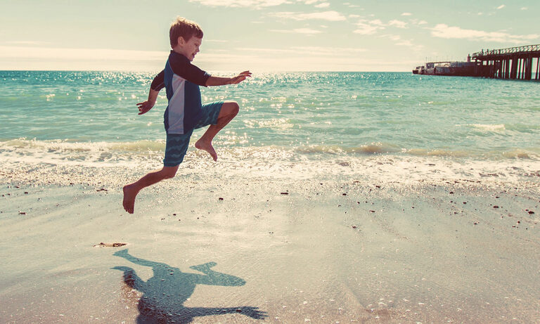 Foto: Junge hüpft am Strand entlang.