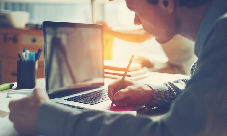 Foto: Mann sitzt vor Laptop und schreibt etwas.